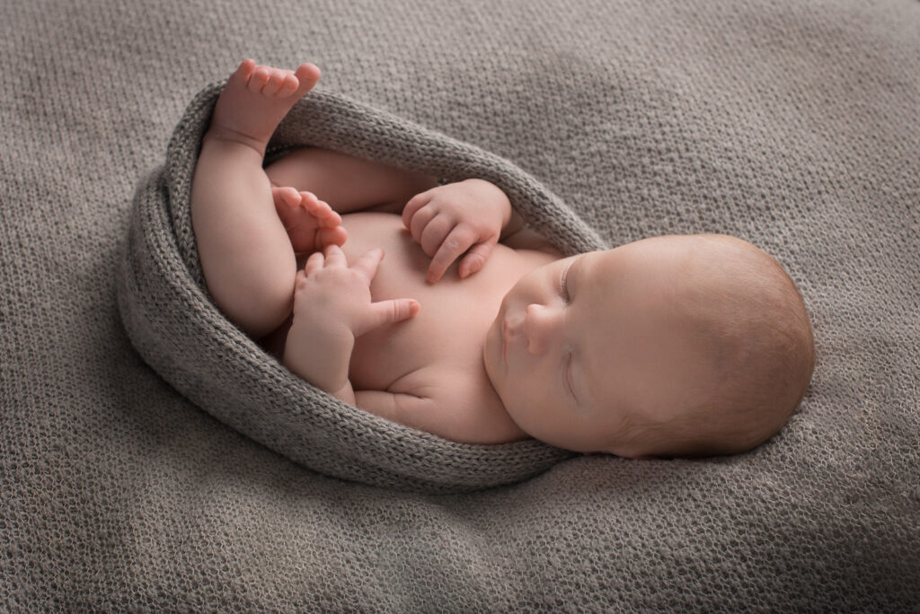 Neugeborenes Baby liegt auf grauer Decke