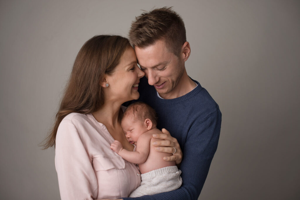 Die Eltern halten die Köpfe zusammen während das Baby auf dem Arm liegt