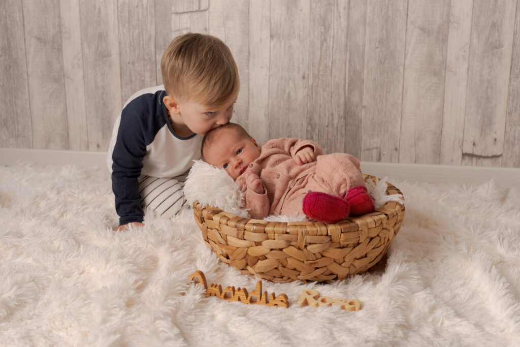 Der große Bruder küsst sein Schwesterchen auf den Kopf beim Neugeborenen - Fotoshooting