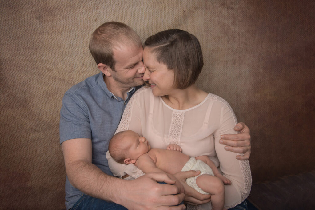 Eltern lächeln. legen die Köpfe zusammen mit Baby im Arm