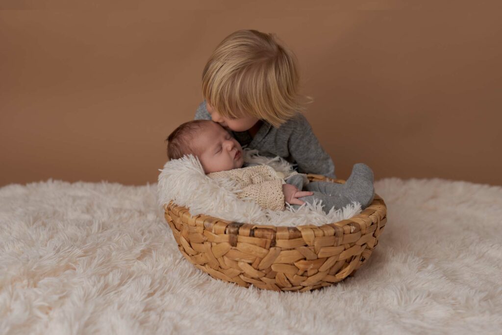 Der große Bruder schaut neugierig in den Korb mit dem neugeborenen Baby 