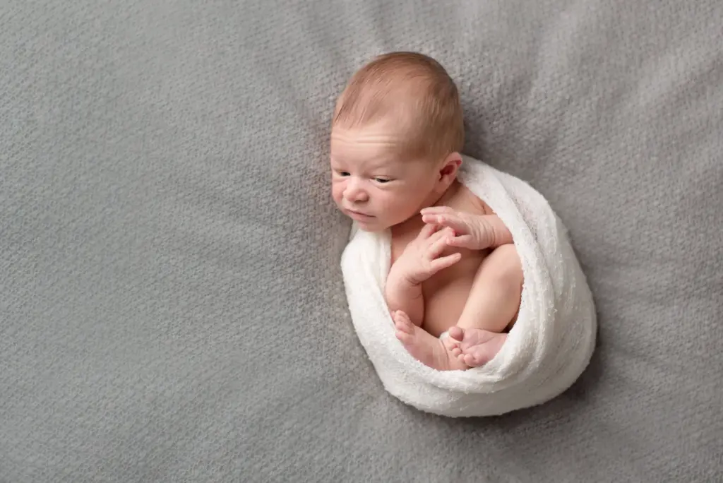 Neugeborenes Baby in weißes Tuch gewickelt, schläft friedlich auf grauem Hintergrund – Neugeborenenfotos Hemmingen