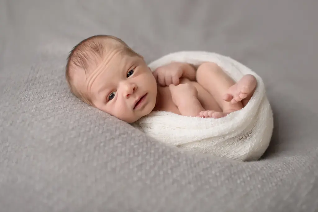 Neugeborenes Baby ruhig schauend, in weißes Tuch gehüllt, Seitenansicht – Neugeborenenfotos Studio Ludwigsburg